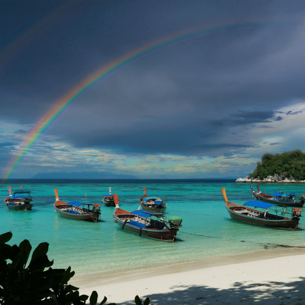 A large Rainbow and cloudy skies over longtail boats at the beach in Koh Lipe Thailand.